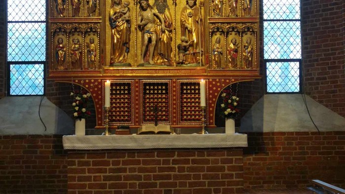 Indviklet alter med religiøse udskæringer og farvede glasvinduer i det indre af en historisk kirke.