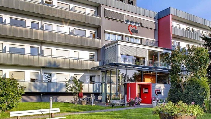 Moderne Wohnanlage mit begrüntem Gartenbereich, Bänken und Sitzgelegenheiten im Außenbereich nahe dem Eingang.