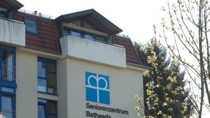 Ein Gebäude mit der Beschriftung *„Seniorenzentrum Bethesda“*, einem Logo und blau gerahmten Fenstern, das in einer grünen Umgebung liegt.