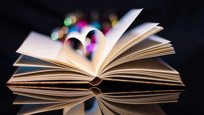 Ein aufgeschlagenes Buch mit einem Herz aus den Seiten, unscharfes Licht im Hintergrund