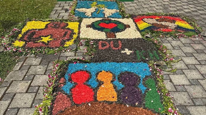 Bunte Blumenmuster, die auf gepflastertem Boden angeordnet sind, mit lebendigen Formen und Buchstaben, die künstlerische Muster bilden.
