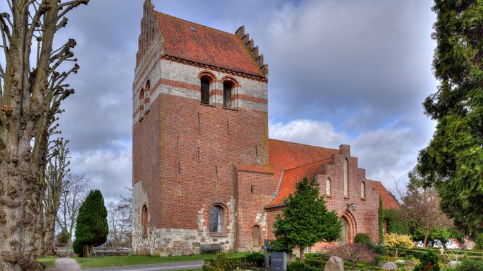 Historisk murstenskirke med et højt tårn og buede vinduer i en rolig, anlagt kirkegård.