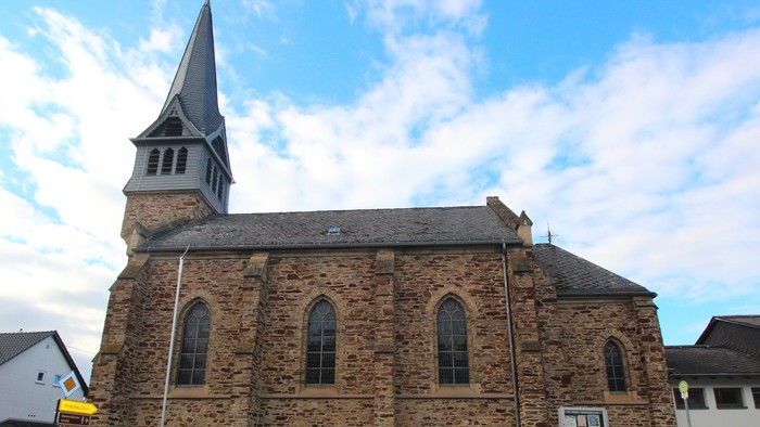 Historische Steinkirche mit hohem Kirchturm und Bogenfenstern unter einem teilweise bewölkten Himmel.