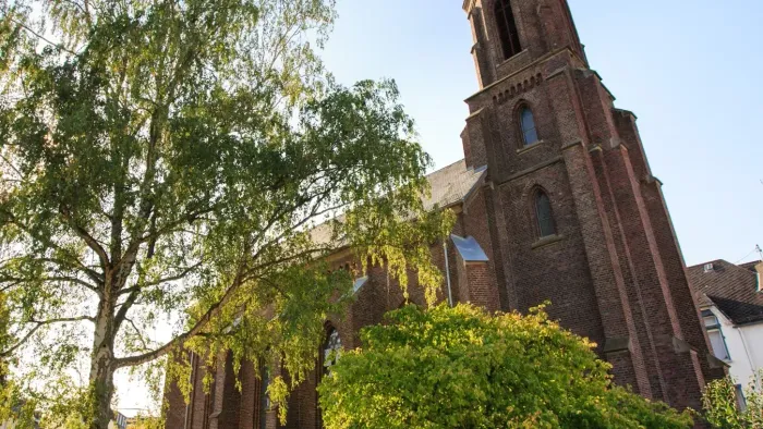 Historische Backsteinkirche mit hohem Turm, umgeben von üppigem Grün unter klarem Himmel.