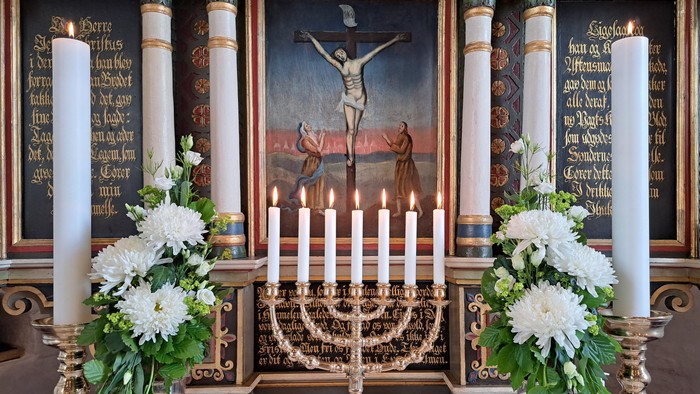Elegant alter med lys, blomsterarrangementer og et maleri af korsfæstelsen med udsmykkede trædetaljer.