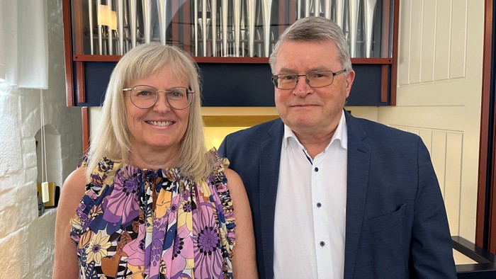To personer smiler til et foto foran et stort pibeorgel.