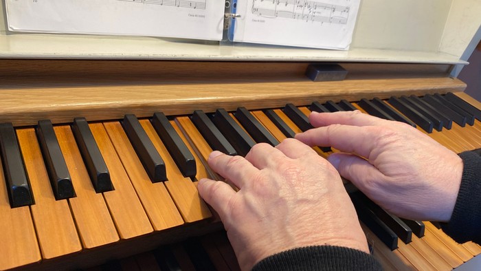 Hænder spiller på et orgel med noder på stand.
