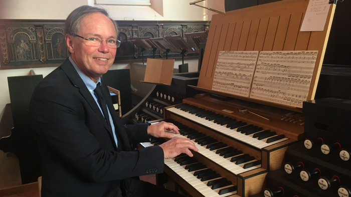 En mand i formelt tøj spiller på et stort orgel i en kirke.