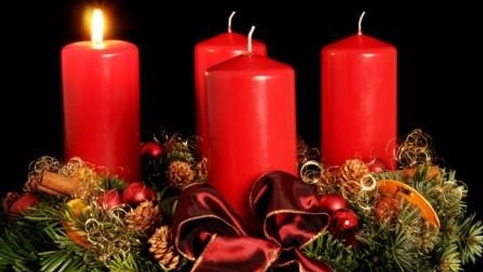 Fire røde lys på adventkrans med grønne gren og røde bærer.