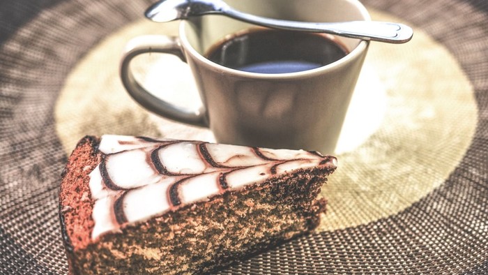 Et stykke kage og en kop kaffe med en ske på et bord.