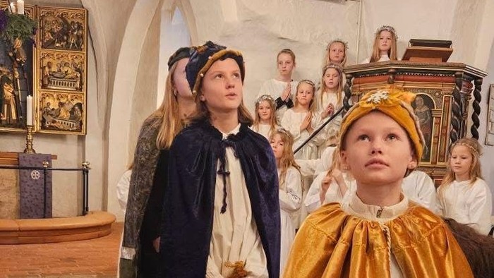 Børn klædt i middelalderkostumer optræder i en kirkelig setting, mens et publikum følger opmærksomt med.