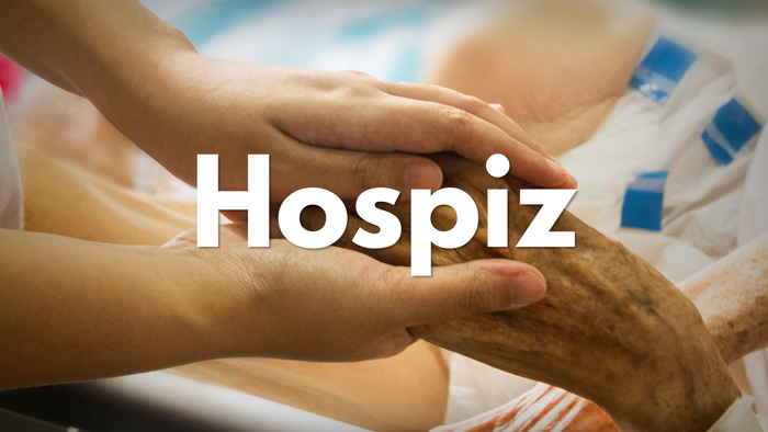 Mitfühlende Hände, die den Arm einer älteren Person in einem Hospiz halten, mit dem Text „Hospiz“ überlagert.