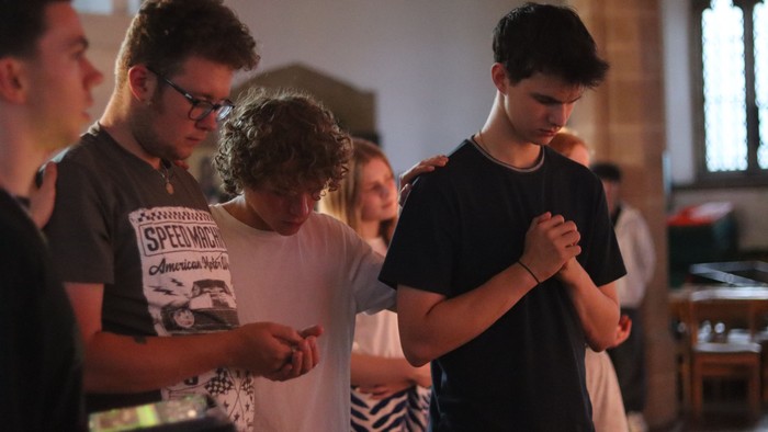 A group of people standing in a church, some looking at their phones.