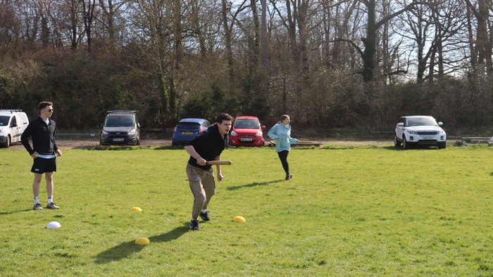 People playing frisbee golf in a grassy field with parked cars in the background.