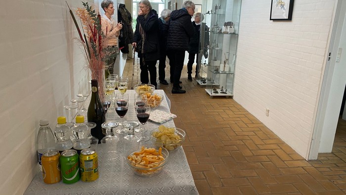 En gruppe mennesker ser udstilling i et galleri med mad og drikkevarer på en bord.