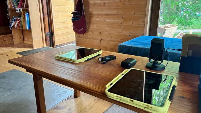 Gemütlicher Arbeitsplatz mit zwei Laptops, einem Telefon und Ladezubehör auf einem Holztisch in der Nähe eines Fensters.