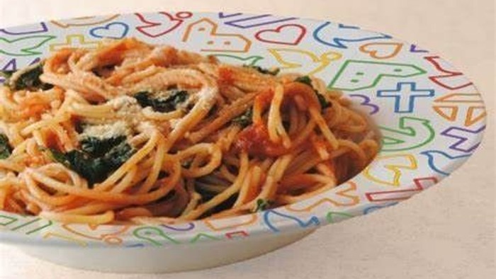 Farverig skål med hjerte-mønster fyldt med spaghetti, tomater, grøntsager og ostesauce.