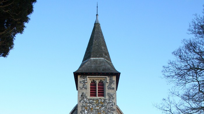Small stone church with red door and steeple, surrounded by grass and trees.