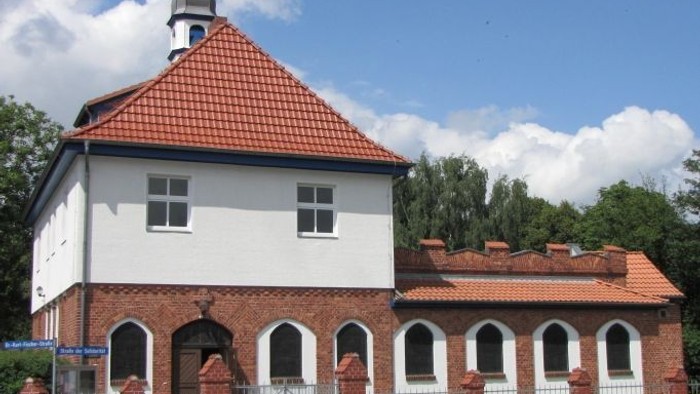 Weißes Gebäude mit rotem Dach und Turm, umgeben von einem Zaun