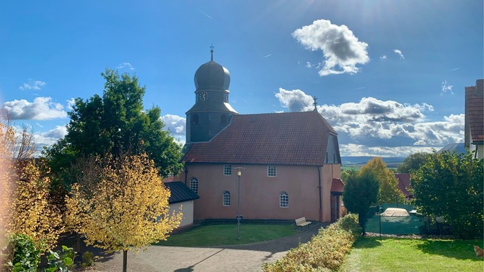 Sonnenbeschienene Kirche mit Kuppel in einem gepflegten, landschaftlich gestalteten Innenhof unter einem strahlend blauen Himmel.