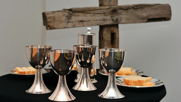 Elegante silberne Kelche und Hostien, arrangiert auf einem Tisch mit einem hölzernen Kreuz im Hintergrund.