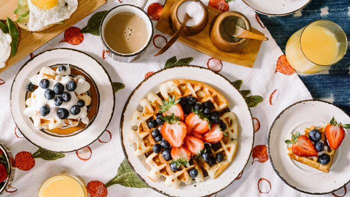 Ein Frühstücksbuffet mit Waffeln, Obst, Eiern und Saften auf einem Tisch