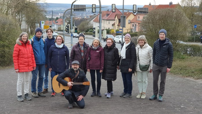 Eine Gruppe von Menschen, die draußen an einer Straßenkreuzung posieren, wobei eine Person Gitarre spielt.