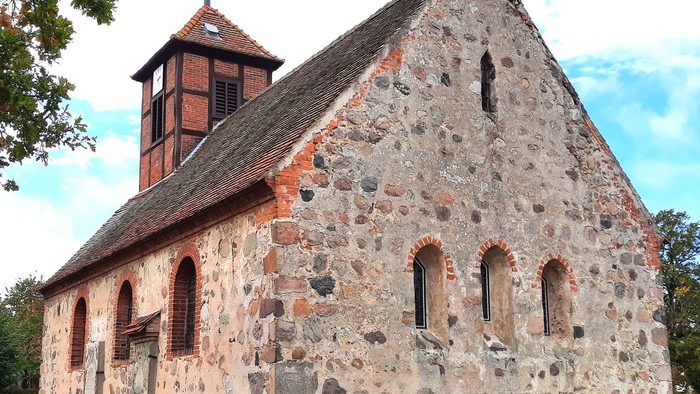 Steinige Kirche mit Turm auf grünem Hügel unter blauem Himmel