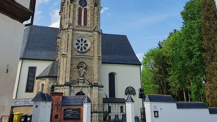 Kirchturm mit Uhr und Kreuzigungsgruppe vor weißem Gebäude