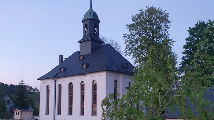 Kirche mit Friedhof und Bäumen im Hintergrund