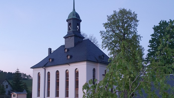 Kirche mit Friedhof und Bäumen im Hintergrund