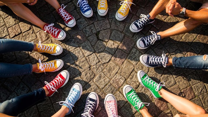 Eine vielfältige Gruppe bunter Sneaker, die im Kreis auf Kopfsteinpflaster angeordnet sind.