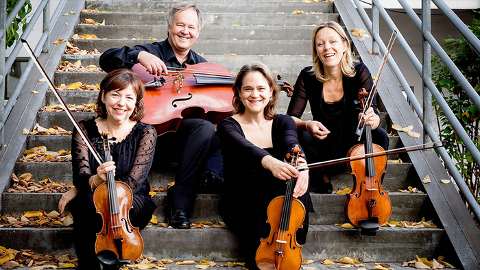 4 Musiker:innen in schwarzer Kleidung sitzen mit ihren Instrumenten - zweimal Violine, Viola und Violoncello - auf einer Treppe.