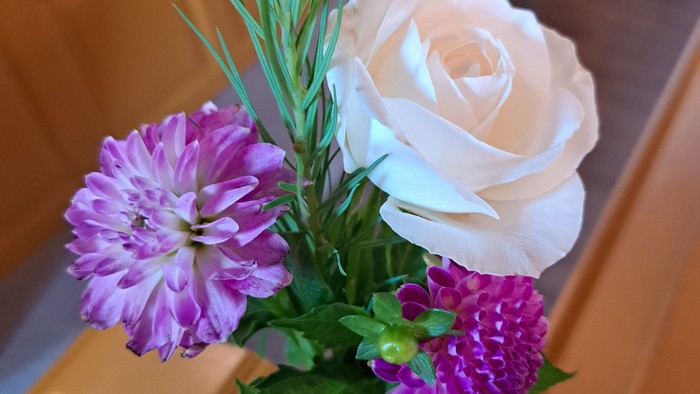 Elegant blomsterarrangement med hvide roser, lilla blomster og grønt løv placeret på træbænke.