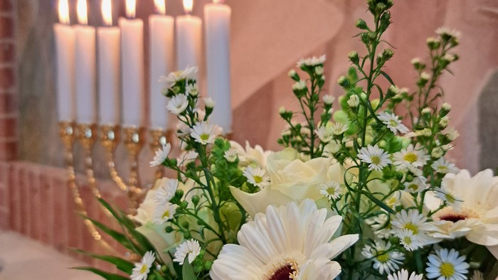 Elegant blomsterarrangement med hvide blomster og grønt ved siden af tændte lys på et bord.