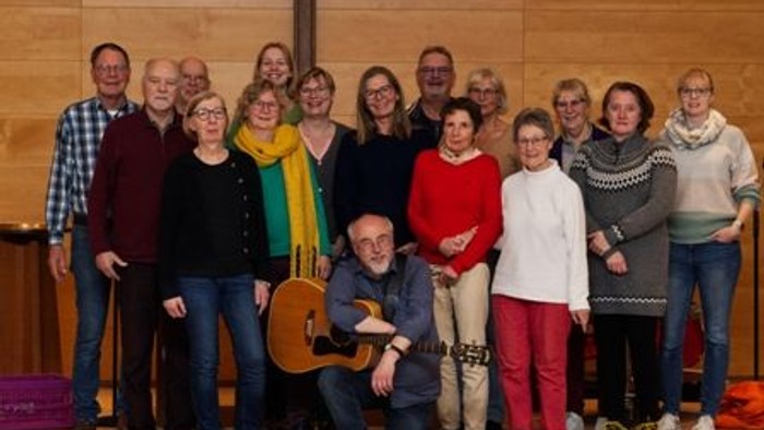 Gruppe von Menschen, die drinnen in einer Kirche in der Nähe eines Kreuzes posieren, wobei eine Person eine Gitarre hält.