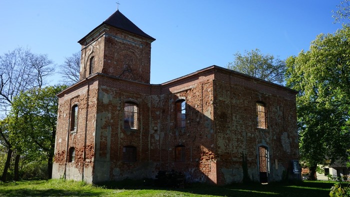 Verfallene Backsteinkirche mit rechteckigen Fensteröffnungen; Auf dem Turm ein Dach mit Kreuz.