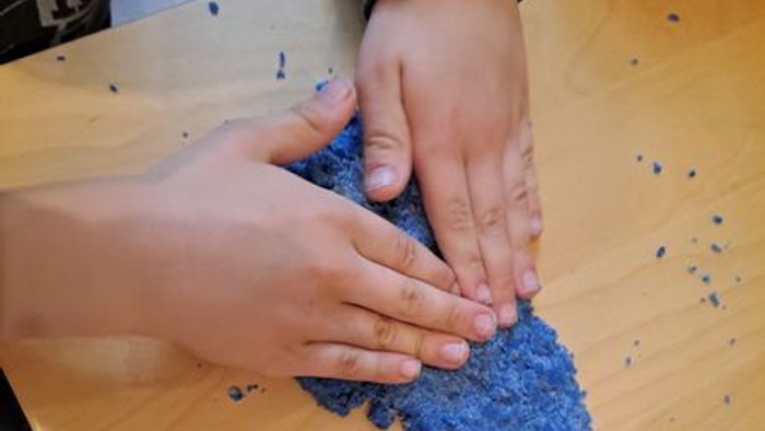 Hände, die blau gefärbten Stoff oder Garn auf einer Holzfläche formen und pressen.