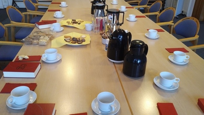 Zeigt eine Tafel mit Kaffeekannen, Kaffeetassen, Keksen und Gesangbüchern