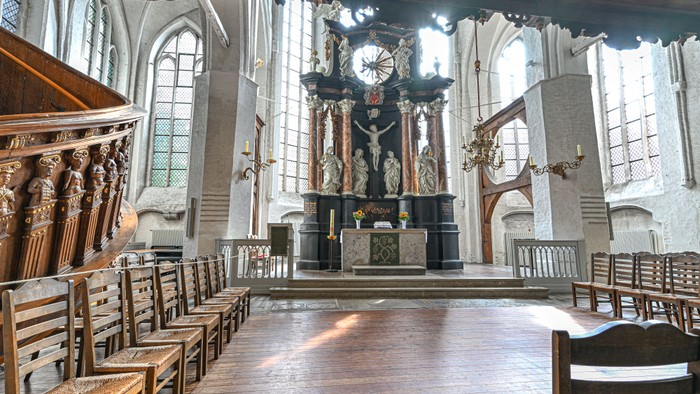 Historisches Kircheninneres mit prunkvollem Altar, hölzernen Kirchenbänken und großen Buntglasfenstern.