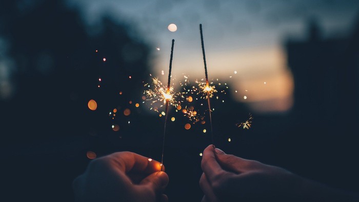 Zwei Hände halten ein Feuerwerk, das in der Dämmerung leuchtet