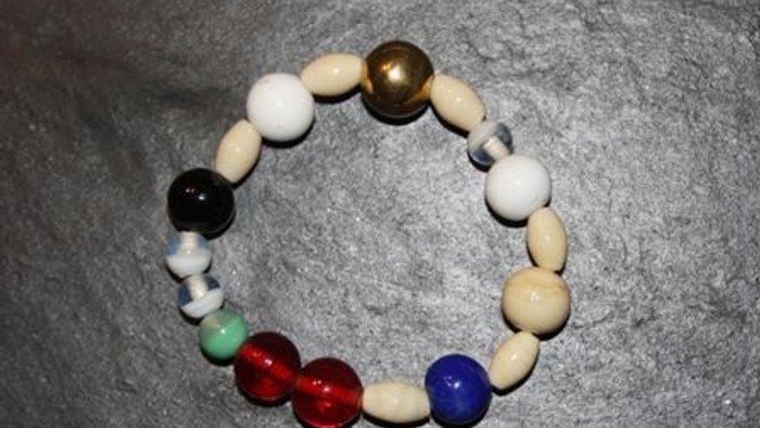 Buntes Perlenarmband mit weißen, roten, blauen, grünen, schwarzen und goldfarbenen Perlen in einem kreisförmigen Muster angeordnet.
