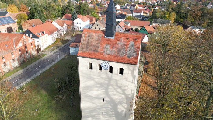 Luftaufnahme einer malerischen Stadt mit einem historischen Uhrturm, umgeben von Gebäuden mit roten Dächern und Grünflächen.