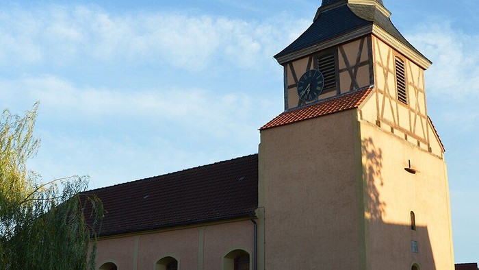 Idyllische Kirche mit hohem Glockenturm und traditionellem Fachwerkstil in einer ruhigen Landschaft.
