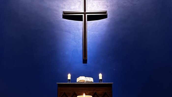 Kerze in rundem Halter unter einem großen Kreuz an der blauen Wand