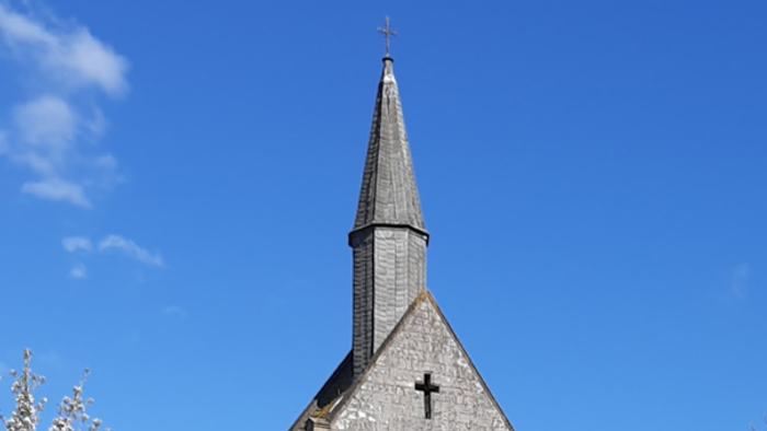 Kirche mit Wiese davor, blühendem Kirschbaum links und blauem Himmel