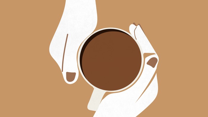 To hænder holder en varm kop kaffe mod en neutral baggrund.