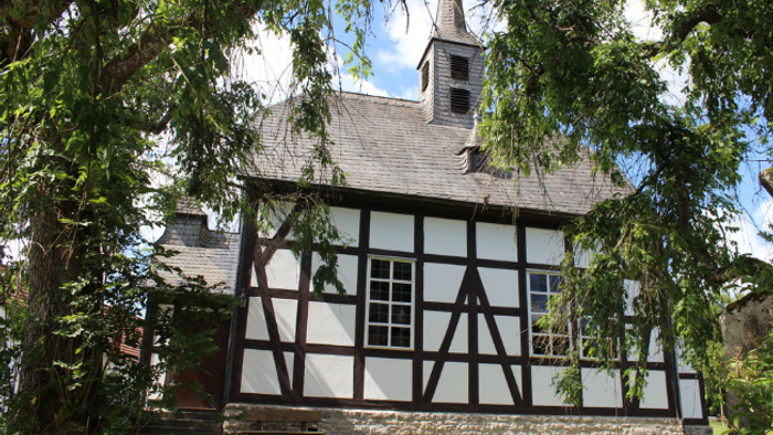 Historisches Gebäude mit Fachwerk, Steinsockel und Glockenturm.