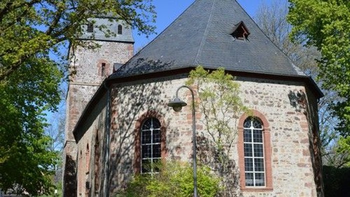 Historische Steinkirche mit efeubewachsenen Mauern und einem hohen Glockenturm neben üppigem Grün.