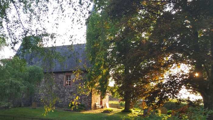 Ein ruhiges Steinhaus, umgeben von üppigem Grün und in warmes Abendsonnenlicht getaucht.
